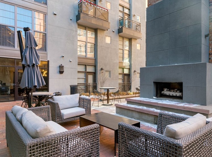 Courtyard Lounge with  Concrete Fireplace Surrounded by Patio Couch and armchairs with Cushions and Coffee Table Next to Building